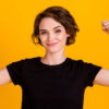 Retrato de uma mulher alegre mostrando os músculos, isolada sobre um fundo de cor amarela.