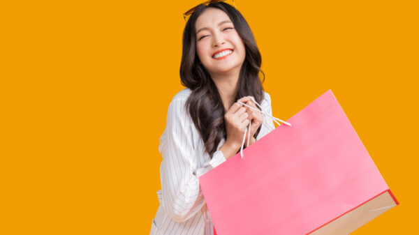 mulher com traços asiáticos sorrindo enquanto segura sacolas de comprar em vendo amarelo