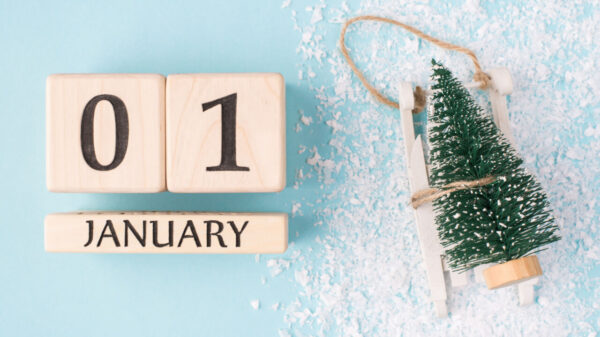 À esquerda está um calendário de madeira marcando o dia primeiro de janeiro e à direita uma árvore de natal pequena em fundo azul