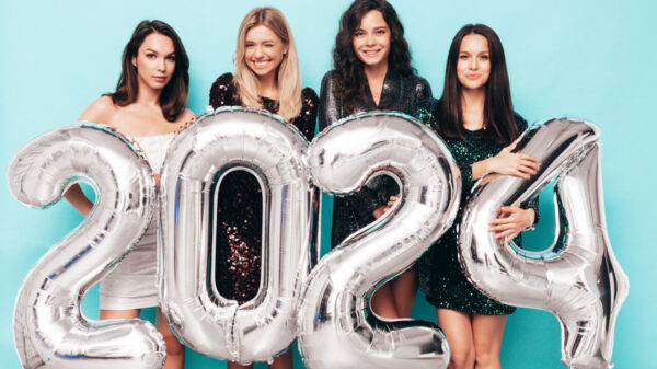 Quatro mulheres comemorando o ano novo, felizes, usando vestidos elegantes de festa, segurando balões prateados de 2024, divertindo-se na véspera de Ano Novo.