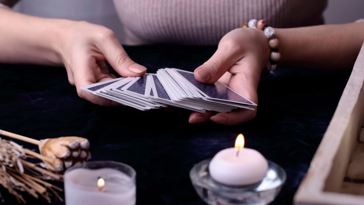 mulher segurando um baralho de cartas de tarot com velas na frente