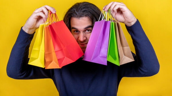Homem em um fundo amarelo mostrando várias sacolas de papel coloridas. Conceitos de compras e presentes.