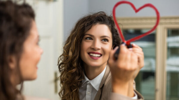 mulher refletida em um espelho desenhando um coração com batom vermelho