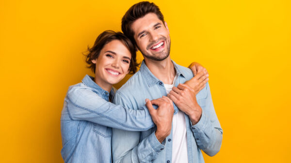 Foto de uma mulher abraçando um homem, desfrutando de um encontro romântico junto a ele, em um fundo de cor amarela isolado.