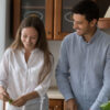 casal feliz temperando salada na cozinha de casa com armários de madeira