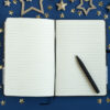 Um diário aberto, uma caneta e estrelas em um fundo azul. Conceito de planejar o ano-novo.