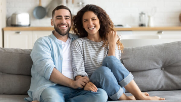 casal sorridente sentados em um sofá cinza na sala de estar da casa