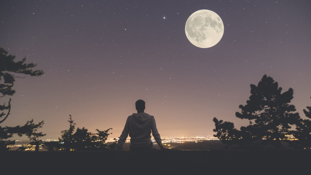 Homem, à noite, observando as luzes da cidade, a lua e as estrelas.