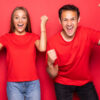 Retrato de duas pessoas (uma mulher e um homem), regozijando-se com algo, usando camisetas vermelhas, em um fundo vermelho.