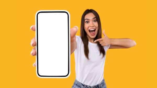 mulher branca com cabelo liso e segurando um celular e apontando para ele em fundo amarelo