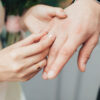 foto das mãos de um casal onde a mão feminina está colocando uma aliança de casamento na mão masculina