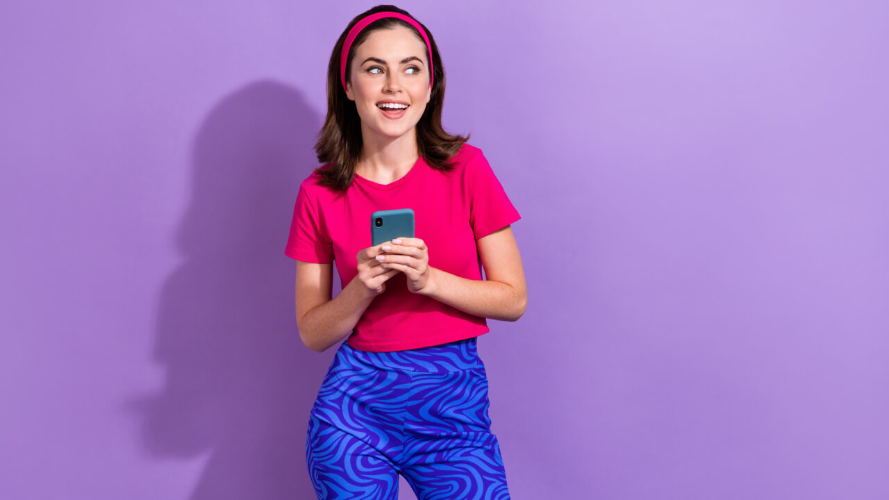 Retrato de uma mulher muito positiva, segurando o celular, isolada em um fundo de cor roxa.
