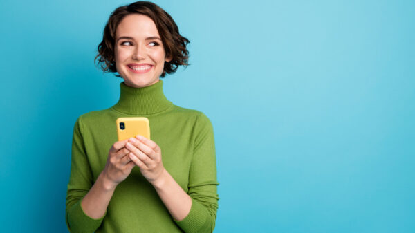 à esquerda está uma mulher vestindo verde sorrindo e com um celular na mão em fundo azul