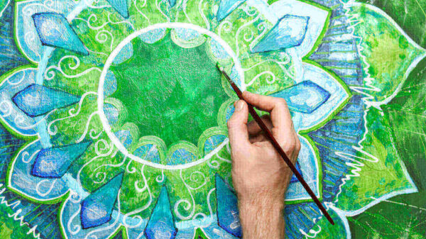 Homem pintando uma mandala verde brilhante, de anahata chakra.