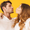 casal vestindo roupa branca e fazendo bico de beijo em fundo amarelo