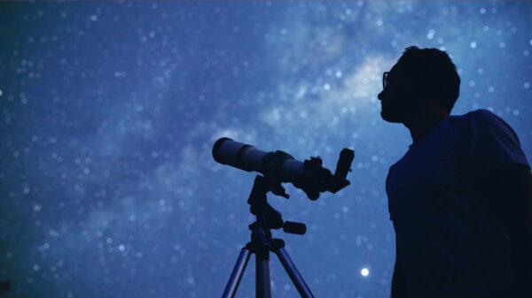 Astrônomo com um telescópio observando as estrelas e a lua.
