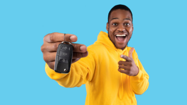 homem jovem negro com um moletom amarelo segurando uma chave de carro na mão esquerda em fundo azul