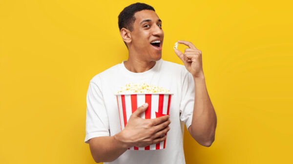 Homem comendo pipoca e assistindo a um filme em um fundo amarelo isolado, satisfeito, sorrindo.