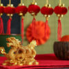 pequeno dragão dourado em cima de uma mesa vermelha e com decoração chinesa desfocada ao fundo