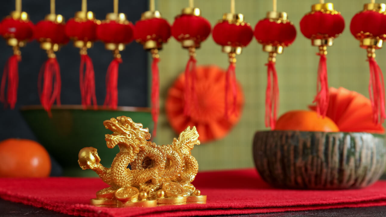 pequeno dragão dourado em cima de uma mesa vermelha e com decoração chinesa desfocada ao fundo