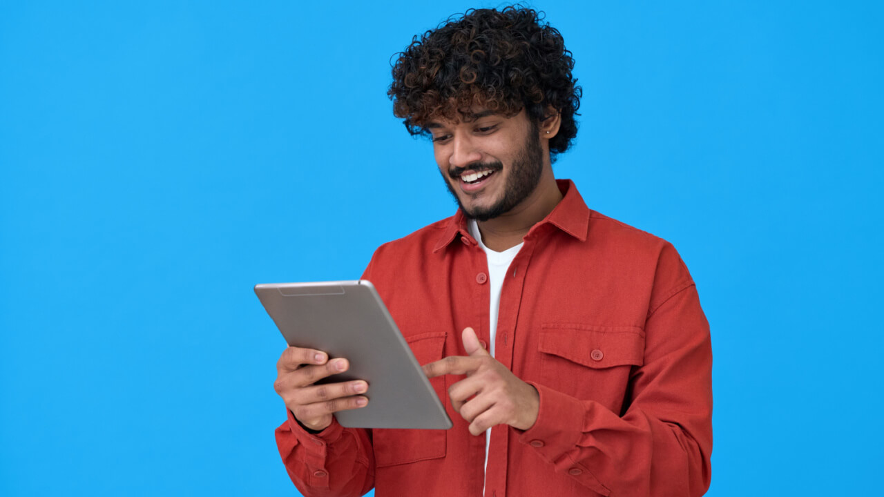 Homem feliz, sorrindo, usando um tablet, isolado em um fundo azul.