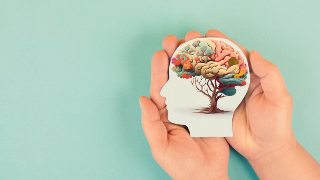 Mãos segurando uma papel em formato de cabeça, cérebro humano com flores.