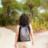 imagem de uma mulher de costas com uma mochila e ela está olhando para uma estrada de dois caminhos em uma floresta