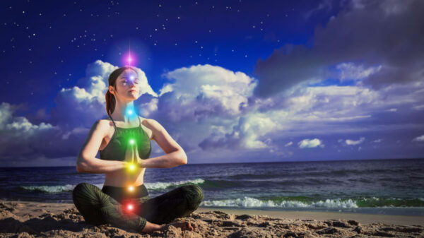 7 chacras. Uma mulher meditando na posição de lótus em um fundo do céu azul escuro e do mar. O conceito de harmonia, cura e calma.