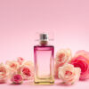 imagem com um vidro de perfume no centro e rosas aos lados em fundo rosa