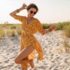 mulher na praia usando vestido amarelo e óculos de sol