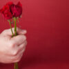 Buquê de rosas vermelhas na mão de um homem, sobre um fundo vermelho.