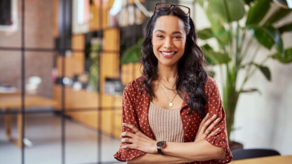 mulher negra sorrindo de braços cruzados em um ambiente que parece ser escritório de trabalho