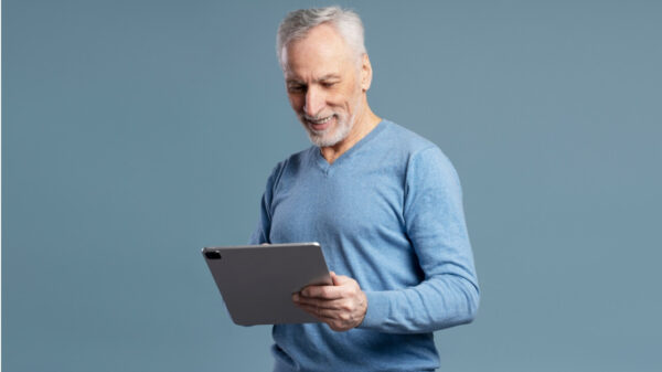 Homem sorrindo, segurando um tablet, isolado em um fundo azul.