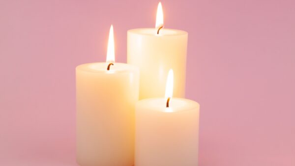 três velas grossas acessas em um fundo rosa