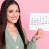 mulher sorrindo e segurando um calendário em fundo rosa