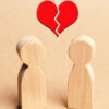 Dois bonecos de madeira e um coração vermelho partido acima deles. Conceito de rompimento de relacionamento; divórcio.