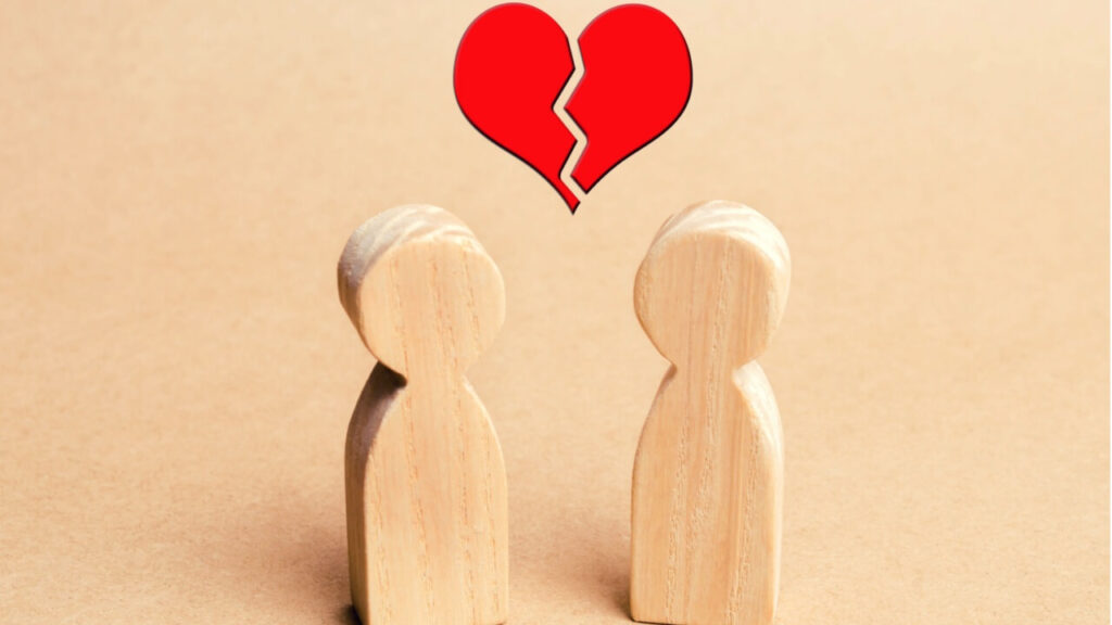 Dois bonecos de madeira e um coração vermelho partido acima deles. Conceito de rompimento de relacionamento; divórcio.