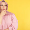 Mulher muçulmana com a mão no rosto e uma expressão pensativa.
