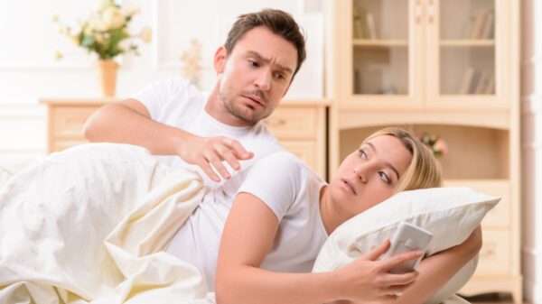 casal deitado na cama com ele tentando olhar o que está no celular dela