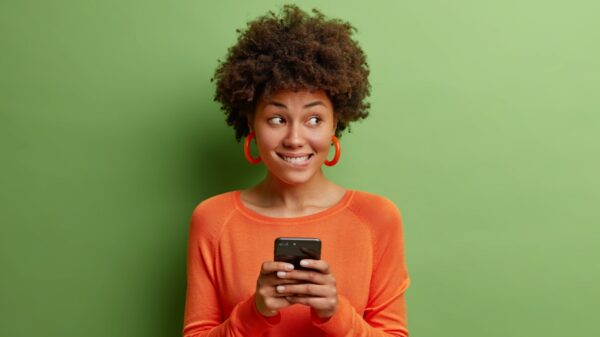 mulher segundo os lábios com os dentes e olhando com o canto de olho enquanto segura um celular em fundo verde