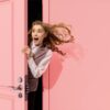 mulher aparecendo em uma porta rosa entreaberta