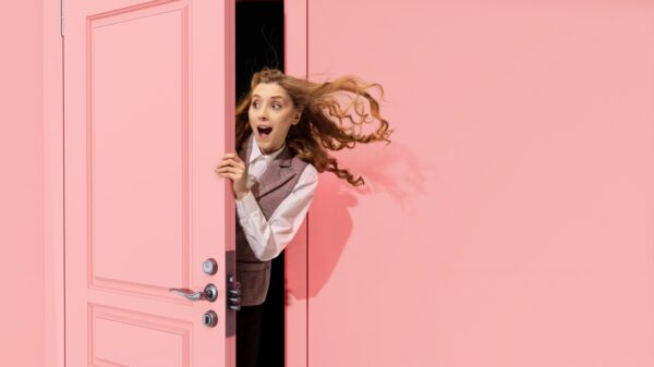 mulher aparecendo em uma porta rosa entreaberta