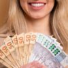 fotografia do sorriso de uma mulher segurando um leque de dinheiro em fundo pêssego