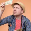 homem olhando uma nota de dolar em fundo laranja