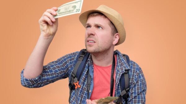 homem olhando uma nota de dolar em fundo laranja