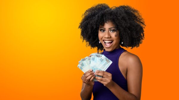 Mulher segurando notas de dinheiro brasileiras, sorrindo, em um fundo gradiente laranja.