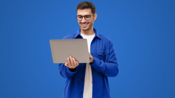 homem segurando um notebook em pé e em fundo azul