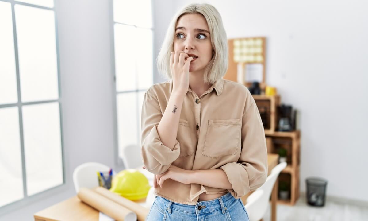 mulher com cara de preocupada, roendo a unha, na frente de um sofá