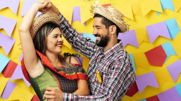 casal fantasiado com roupas de festa junina na frente de um fundo colorido com bandeirinhas juninas
