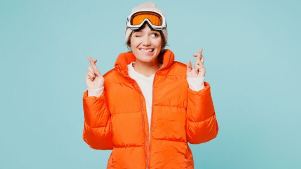mulher com roupas de frio laranja cruzando os dedos e em um fundo azul